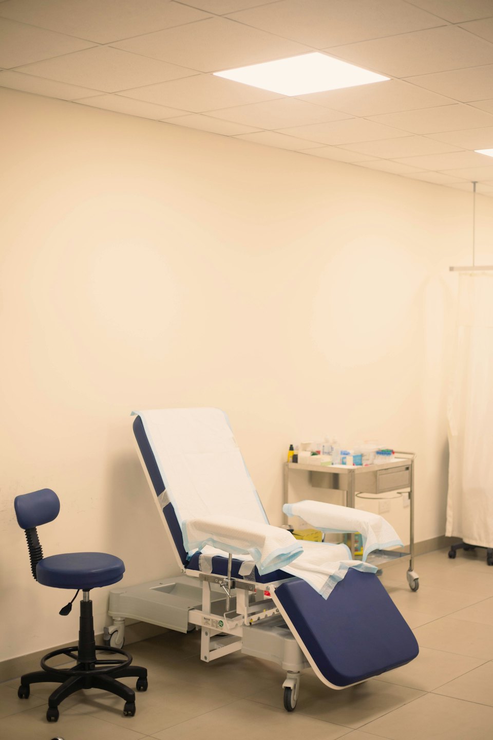 Salle d'examen médical vide avec chaise et chariot bleus et blancs.