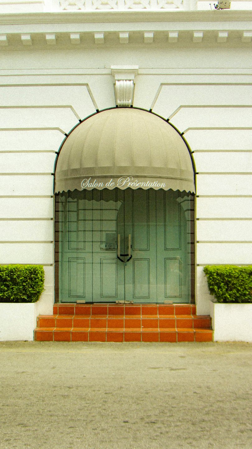 Entrée classique d'un bâtiment blanc avec des portes vertes et un auvent arqué.